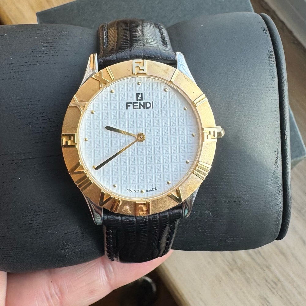 FENDI SWISS MADE, white face watch with gold accents and black lea band.